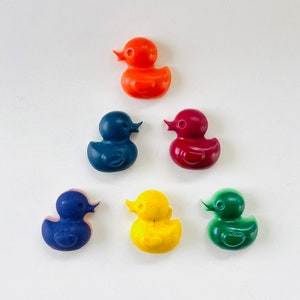 May include: Six small rubber duck crayons in different colors: red, blue, yellow, green, dark blue, and orange. The crayons are shaped like rubber ducks.
