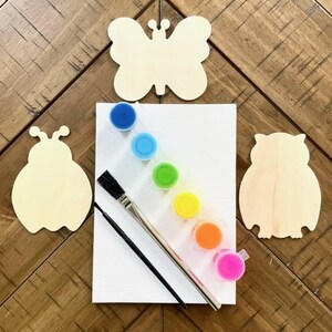 May include: A wooden craft kit with a butterfly, ladybug, and owl shape. The kit includes six small paint pots in rainbow colors, a paintbrush, and a small paintbrush.