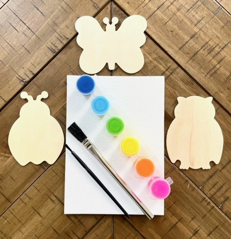 May include: A wooden craft kit with a butterfly, ladybug, and owl shape. The kit includes six small paint pots in rainbow colors, a paintbrush, and a small paintbrush.