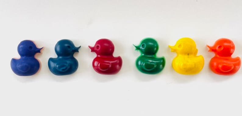 May include: Six rubber duck crayons in different colors: blue, dark blue, red, green, yellow, and orange. The crayons are shaped like rubber ducks.