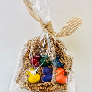 May include: A clear plastic bag filled with brown crinkle paper and six colorful crayon shaped like ducks. The crayons are red, yellow, green, blue, orange, and purple.