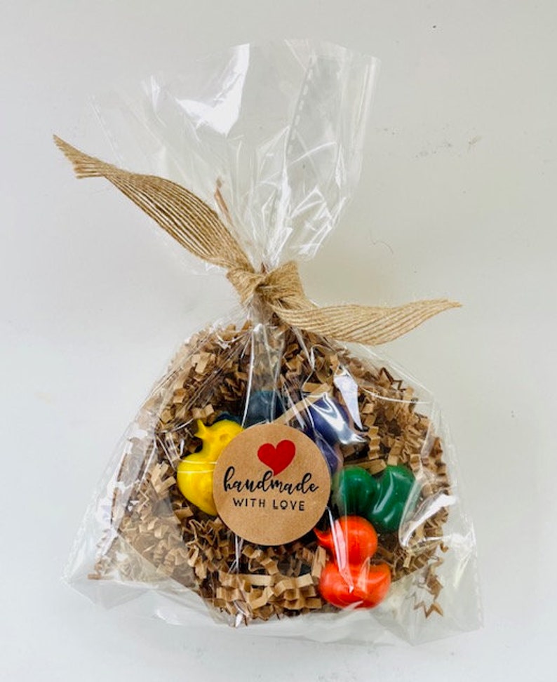 May include: A clear plastic bag filled with brown paper shreds and colorful crayons. The crayons are shaped like birds and have a brown paper tag with a red heart and the text "handmade with love".