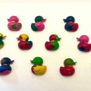 May include: A collection of 12 colorful rubber duck crayons. The crayons are in various shades of pink, red, blue, green, and yellow. Each crayon is shaped like a rubber duck with a detailed design.
