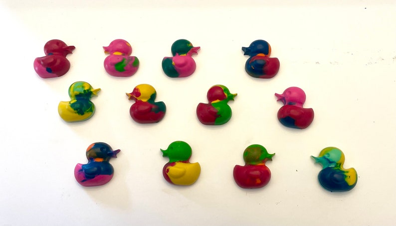 May include: A collection of 12 colorful rubber duck crayons. The crayons are in various shades of pink, red, blue, green, and yellow. Each crayon is shaped like a rubber duck with a detailed design.