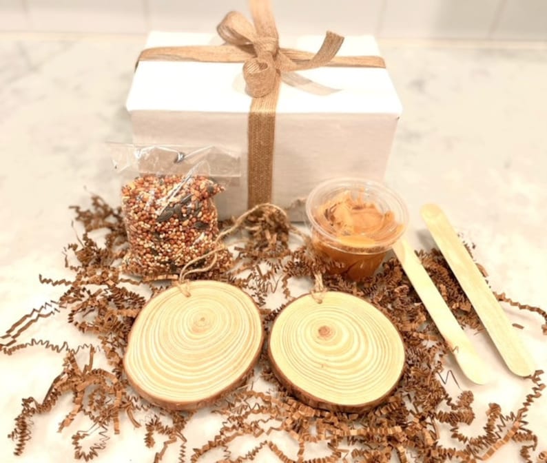 K&ouml;nnte beinhalten: Eine Geschenkbox gef&uuml;llt mit Bastelbedarf zum Herstellen von Vogelh&auml;uschen. Die Box enth&auml;lt zwei Holzscheiben, eine T&uuml;te Vogelfutter, einen kleinen Beh&auml;lter mit Erdnussbutter und zwei Holzst&auml;bchen.