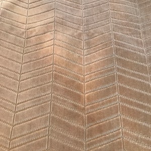 May include: A close-up of a beige fabric with a herringbone pattern. The fabric has a subtle sheen and a soft texture.