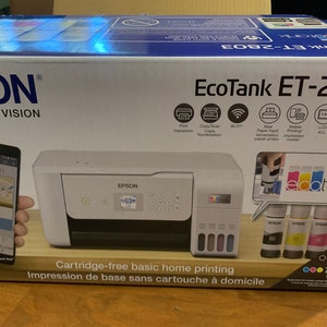 Pode incluir: Impressora Epson EcoTank ET-2803 na embalagem original. A caixa é branca e azul, com a impressora em destaque. Inclui impressão, cópia, digitalização, Wi-Fi e impressão móvel. Inclui frascos de tinta para impressão sem cartuchos.