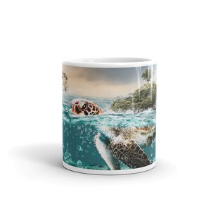 May include: White ceramic coffee mug featuring a sea turtle swimming in the ocean. The mug has a wrap-around design with a detailed illustration of the turtle, water, and a small island. The turtle's head is visible above the water.