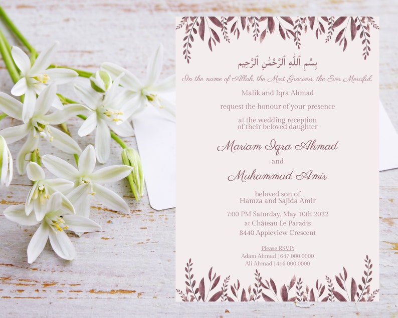 May include: A wedding invitation with floral accents and text in English and Arabic. The invitation is a soft beige color with burgundy-colored leaves and text. White flowers are in the foreground.