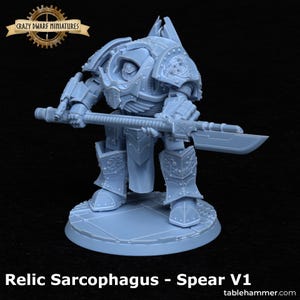 May include: A light blue miniature of a Relic Sarcophagus, holding a spear. The figure is heavily armored with intricate details, standing on a circular base. The text "Crazy Dwarf Miniatures" is at the top, and "Relic Sarcophagus - Spear V1" is at the bottom.