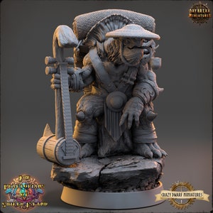 May include: A gray, detailed miniature of a turtle-like creature wearing a conical hat and holding a large, wooden instrument. The creature is wearing a belt with a round buckle and has a backpack on its back. The miniature is standing on a gray, rocky base.