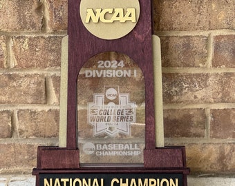 May include: A wooden trophy with a gold NCAA logo, the text "2024 DIVISION I", and "NATIONAL CHAMPION". The trophy also features a clear acrylic insert with the NCAA College World Series logo.