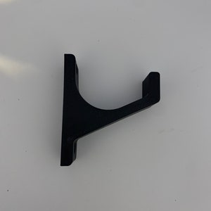 May include: A black plastic wall mount hook with a curved arm. The hook is designed to hold items like coats, hats, or bags.