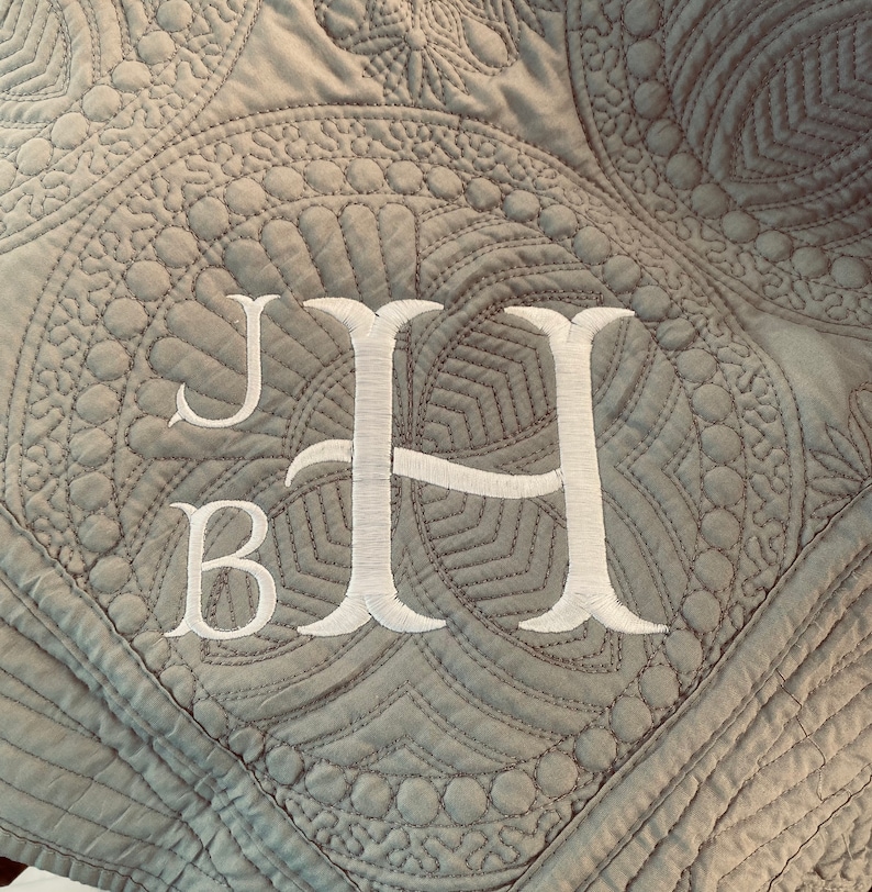 Op de afbeelding: Een grijs gestikt deken met een wit geborduurd monogram "JB" in een schrijfletter.