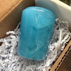 Peut inclure: Un gobelet cylindrique présentant une finition brillante avec un motif marbré composé de tourbillons bleu ciel vif et blancs. L'objet est niché dans une boîte en carton remplie de papier déchiqueté blanc, offrant une présentation sécurisée.