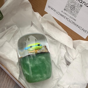 Könnte beinhalten: Ein klarer Harz-Briefbeschwerer mit einer Teenage Mutant Ninja Turtle-Figur. Der Sockel ist marmoriert grün, und die Oberseite ist eine klare Kuppel. Präsentiert in einem Karton mit weißem Seidenpapier.