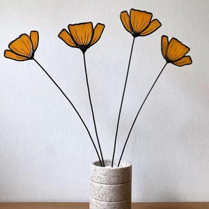 May include: Four orange glass flowers with black stems in a white and gray textured vase.