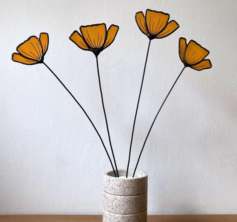 May include: Four orange glass flowers with black stems in a white and gray textured vase.