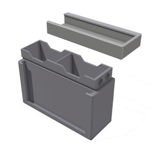 May include: A gray, modular storage container with a rectangular base and a separate, matching tray. The container has two internal compartments and two small holes on the top. The design is simple and modern.
