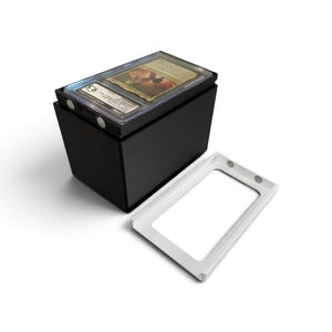 K&ouml;nnte beinhalten: Eine schwarze, rechteckige Aufbewahrungsbox mit magnetischem Deckel, die eine einzelne bewertete Sammelkarte in einer transparenten Kunststoffh&uuml;lle enth&auml;lt. Die H&uuml;lle tr&auml;gt ein CGC-Etikett mit der Note 9,5. Ein separater wei&szlig;er Rahmen liegt daneben.