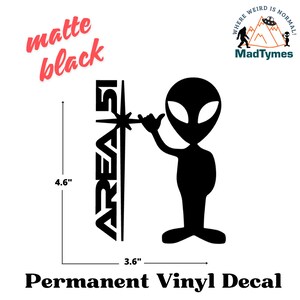 May include: A black and white vinyl decal of an alien with the text "AREA 51" and a star. The decal is 4.6 inches tall and 3.6 inches wide.