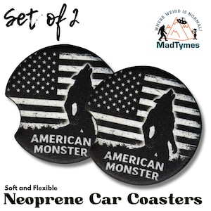 May include: Set of two black neoprene car coasters. Each coaster features a distressed American flag design with a howling wolf silhouette and the text "AMERICAN MONSTER". The coasters are soft and flexible.