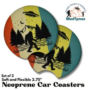 May include: Set of two 2.75 inch round neoprene car coasters with a retro design. The coasters feature a yellow, orange, and blue striped background with a silhouette of Bigfoot walking through a forest with a UFO flying overhead. The text "Where Weird Is Normal! MadTymes" is printed on the coasters.