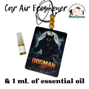 May include: A black car air freshener with a Dogman graphic, a full moon, and forest background. Includes a small bottle of essential oil. The text "Car Air Freshener" and "Dogman" are visible. The MadTymes logo is also present.