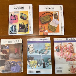 May include: Five sewing pattern envelopes for bags and accessories. Top row: McCall's M4851 and M5824. Bottom row: Vogue 7531, Simplicity 4391, and Simplicity 2201. Each envelope displays illustrations or photographs of finished bags in various colors and styles.