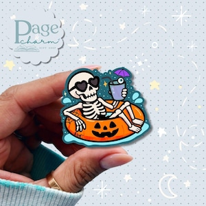 May include: A die-cut sticker featuring a white skeleton wearing black heart-shaped sunglasses, relaxing in an orange jack-o'-lantern pool float. The skeleton holds a purple drink with a straw and a small umbrella, surrounded by blue water splashes.