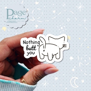 May include: A white die-cut sticker featuring a black line drawing of a cat viewed from behind with its tail raised. The text "Nothing butt you" is printed in black, rounded lettering to the left of the cat illustration on the sticker surface.