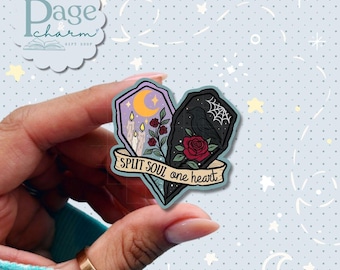 May include: A die-cut sticker featuring two halves of a coffin shape joined together. The left side shows a yellow crescent moon, candles, and red roses on a purple background. The right side features a black raven, a spiderweb, and a red rose.