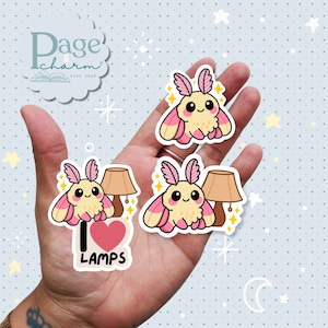 May include: A collection of cute moth stickers with pink and yellow wings, smiling faces, and a lamp design. One sticker reads "I Love Lamps" with a pink heart. The stickers are on a light blue background with stars.