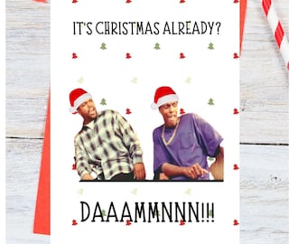 May include: A white Christmas card with a photo of two men wearing Santa hats. The text on the card reads "It's Christmas already? DAAAMMN!!"