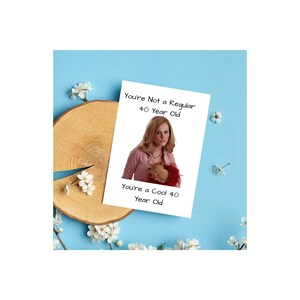 May include: A white card with the text "You're Not a Regular 40 Year Old. You're a Cool 40 Year Old." A woman with blonde hair is pictured on the card. She is wearing a pink shirt and holding a stuffed animal.