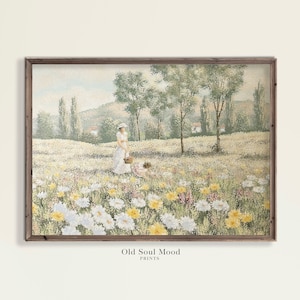 Op de afbeelding: Een ingelijste print van een pastorale scène met een vrouw in een witte jurk en hoed, met een mand in een veld vol wilde bloemen. Het kunstwerk heeft een vintage uitstraling, met een houten lijst en de tekst "Old Soul Mood PRINTS" onderaan.