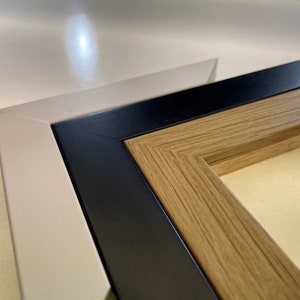 May include: Close-up of a triple matted picture frame with a light beige outer frame, a black middle frame, and a wood-toned inner frame.