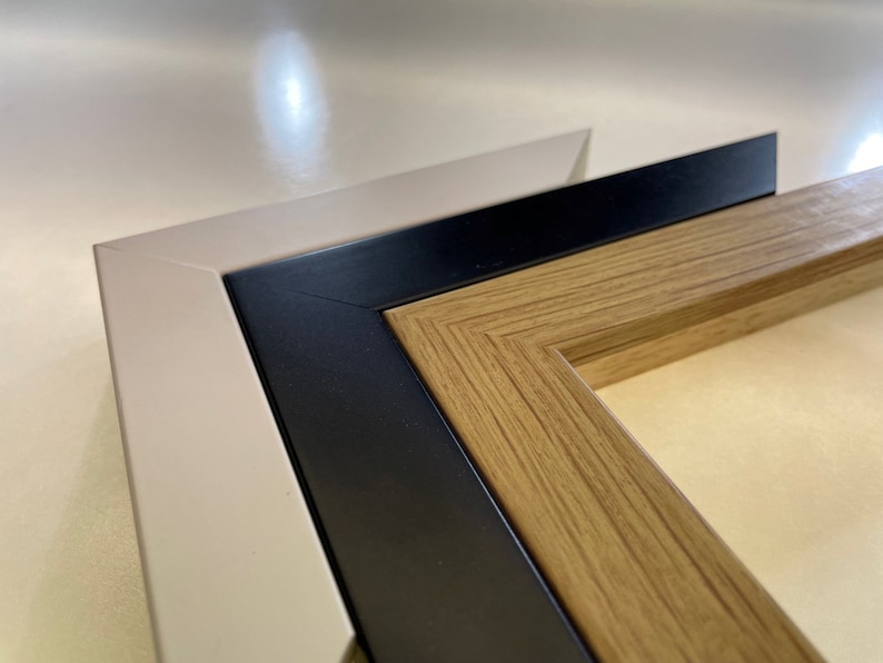 May include: Close-up of a triple matted picture frame with a light beige outer frame, a black middle frame, and a wood-toned inner frame.