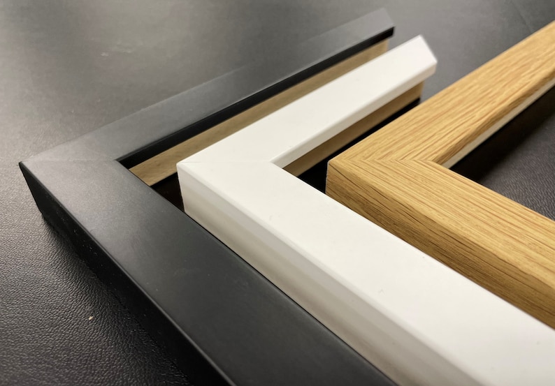 May include: Three picture frames, one black, one white, and one wood, are stacked on top of each other. The frames are all different sizes and have different styles.