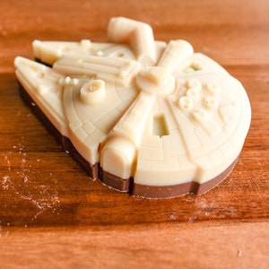 May include: A white chocolate Millennium Falcon spaceship replica on a wooden surface.