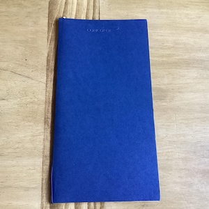 May include: A closed, cobalt blue booklet with the word "CONCORDE" printed at the top. The booklet is rectangular and has a textured surface. The booklet is lying on a light brown wooden surface.