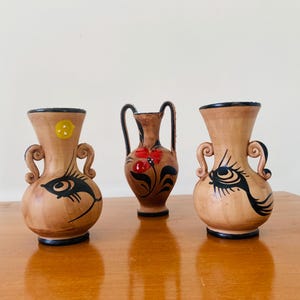 May include: Three small ceramic vases with painted designs. The vases are brown with black and white painted designs. One vase has a red and black floral design.