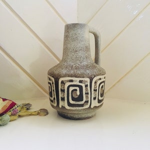 May include: A brown and white ceramic vase with a geometric design. The vase has a rounded body and a handle.