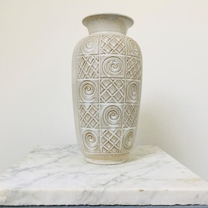 May include: A white ceramic vase with a geometric pattern of squares and spirals. The vase is sitting on a marble surface.