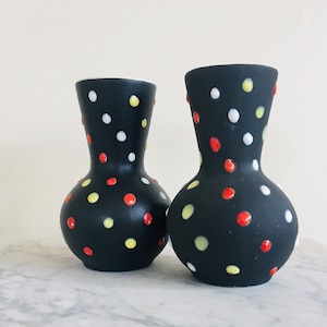 May include: Two black ceramic vases with a polka dot pattern in red, yellow and white.