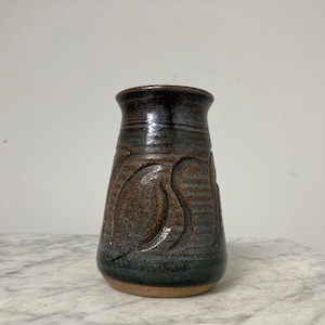 May include: A small, dark brown and blue ceramic vase with a textured, abstract design. The vase has a rounded base and a slightly flared opening.
