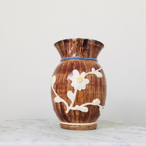 May include: A brown ceramic vase with a white floral design. The vase has a ruffled top and a blue band around the middle.
