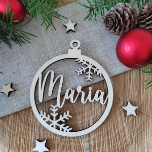 K&ouml;nnte beinhalten: Ein h&ouml;lzerner Weihnachtsbaumschmuck in Form einer Kugel mit dem Namen "Maria", der in einer Schreibschrift ausgeschnitten ist. Der Schmuck ist mit Schneeflocken verziert und hat eine Schnur zum Aufh&auml;ngen.