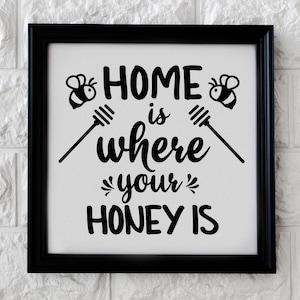 Puede incluir: Un letrero en blanco y negro con el texto "Home is where your honey is" con dos ilustraciones de abejas a cada lado del texto.