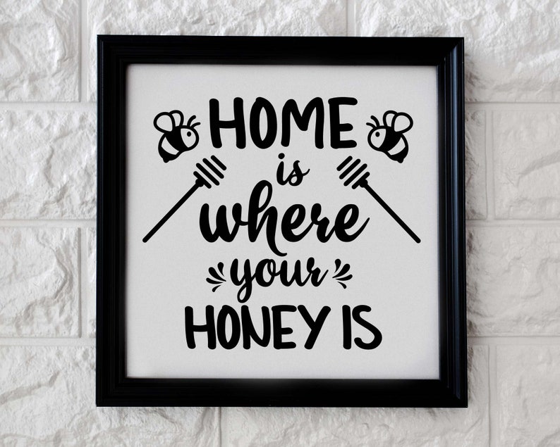 Puede incluir: Un letrero en blanco y negro con el texto "Home is where your honey is" con dos ilustraciones de abejas a cada lado del texto.